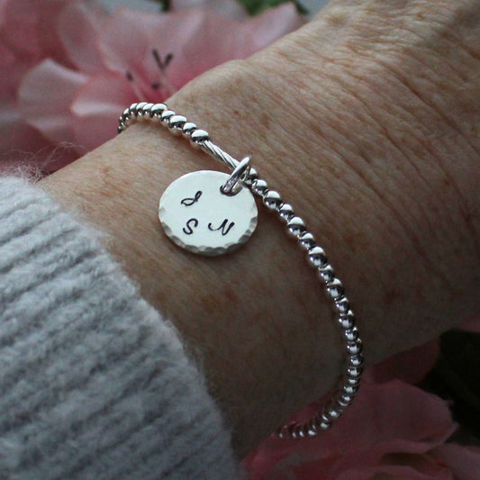 Silver bracelet with a round tag on a wrist against a pink floral background