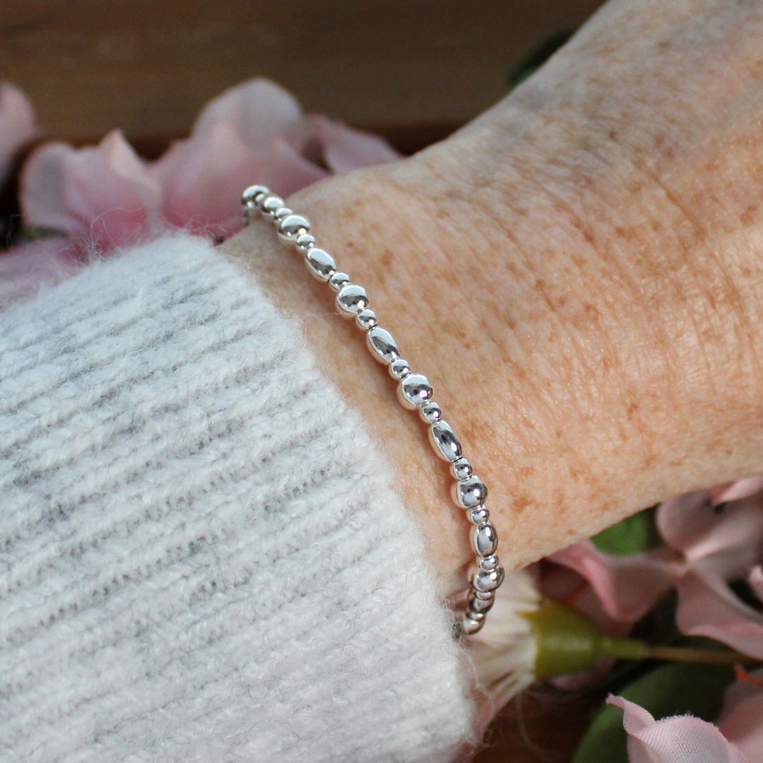 Silver bracelet on a wrist with a blurred floral background