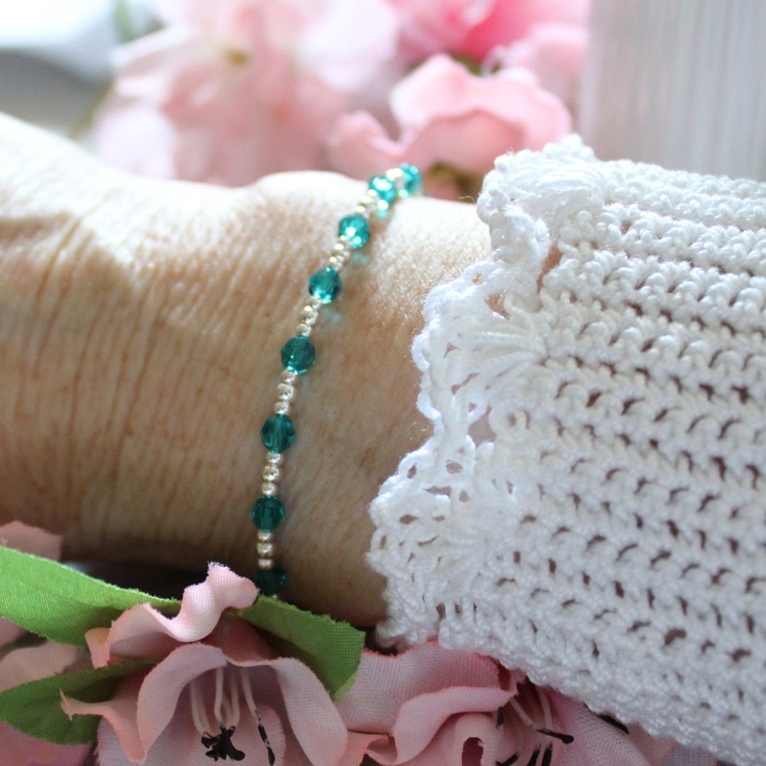 Close-up of a bracelet with green beads on a textured surface with flowers in the background