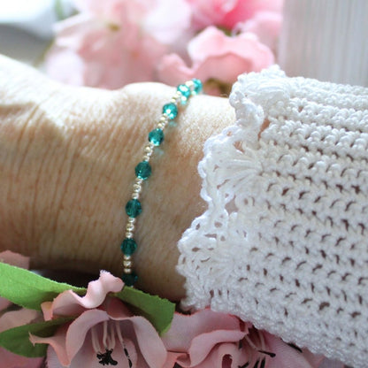 Close-up of a bracelet with green beads on a textured surface with flowers in the background